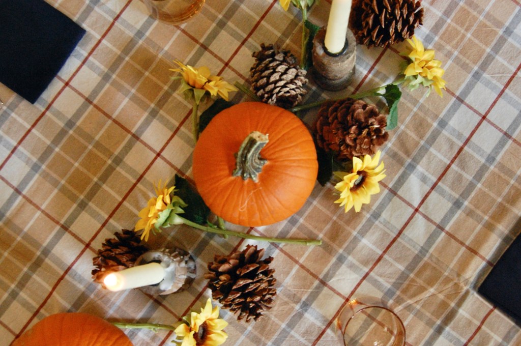 overhead view of thanksgiving table with tan plaid cloth, pumpkins and sunflowers