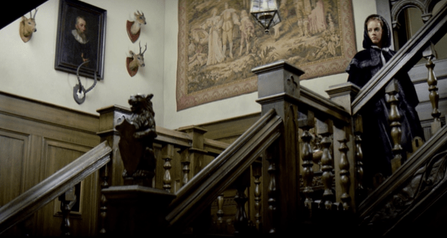 Cinderella stands at the top of a wooden staircase, looking downwards